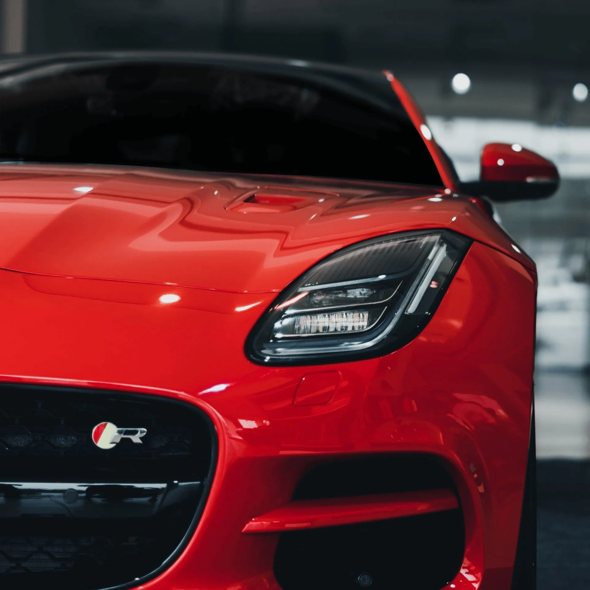 Red Jaguar sports car, close-up front view. Sleek design, black accents, indoor setting.