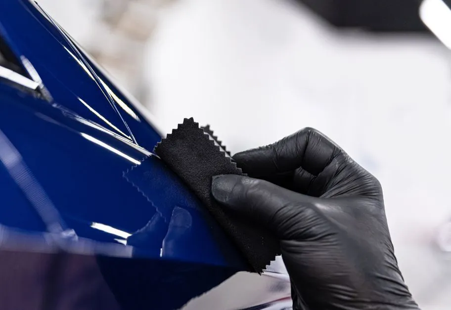 Gloved hand applying a coating to a shiny blue car surface with a black applicator pad.