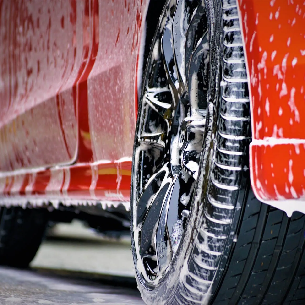 Red car being washed; soapy water on tire and body.