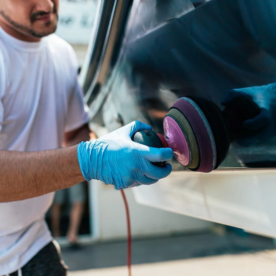 Person in blue gloves polishes a boat hull with a power buffer; close-up.