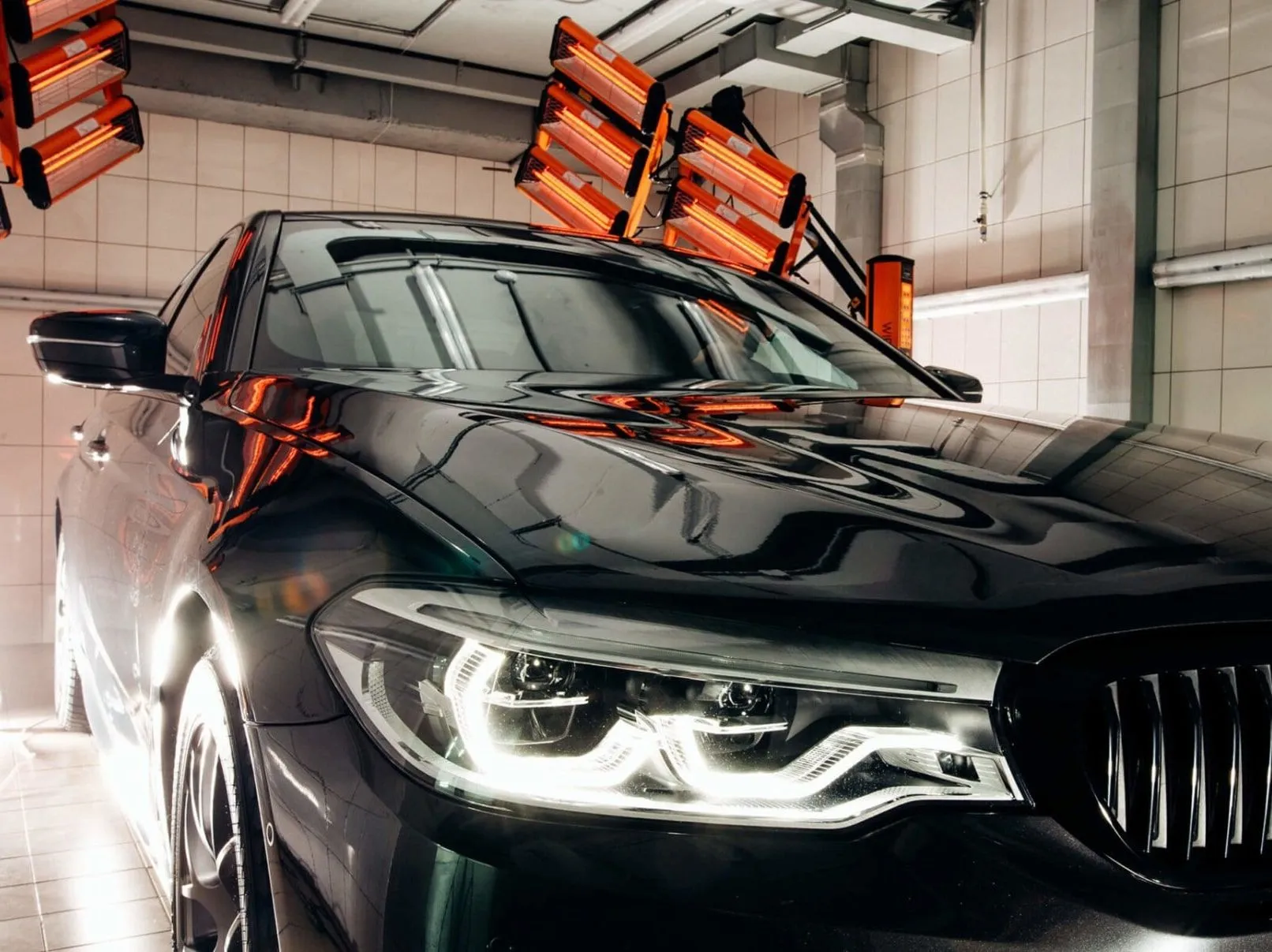Black car under red heat lamps in a car detailing bay.